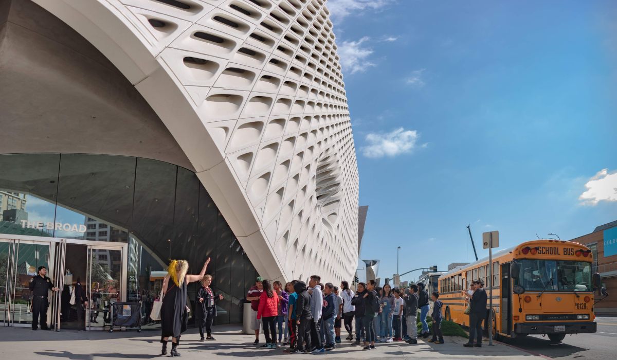 A group of students standing outside of The Broad. They were dropped off by a yellow school bus.