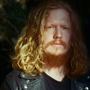 Musician Dave Harrington with long auburn hair and beard, wearing a leather jacket