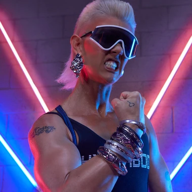  HyperBody in a dark bodysuit with chrome accessories and large sunglasses posing in front of neon lights