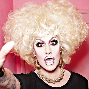 Jackie Beat in full drag makeup and a blonde wig against a pink background