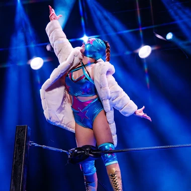 Lucha VaVoom performer in a sequined costume and fur coat on a wrestling ring rope