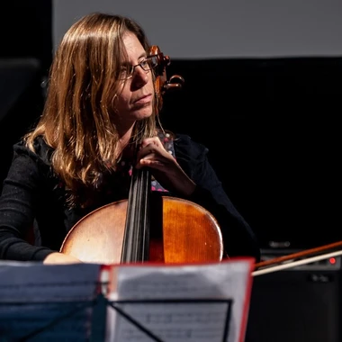 Musician Maggie Parkins playing cello on a darkened stage