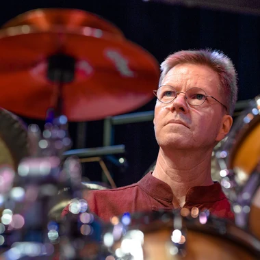 Alex Cline, wearing glasses, sitting behind a drum set