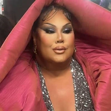 Big Mama Tama, drag queen, dressed in a silver sparkle top with a soft pink pillow-like blanket or jacket draped over her head
