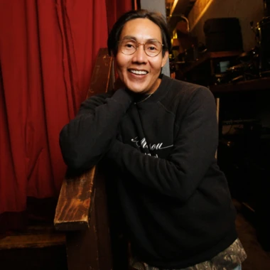 Brian Bahe, wearing round wire-rimmed glasses and a black sweater, smiling.