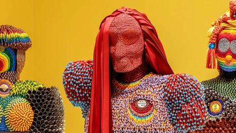Exhibition photo of beaded figurines on yellow background