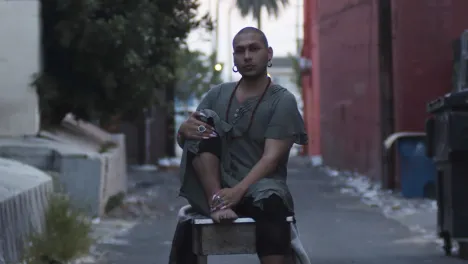 Man sitting on a stool in the middle of an alley.