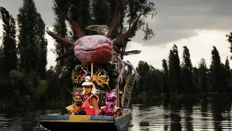 Three women sitting in an axolotl-shaped boat on a pond