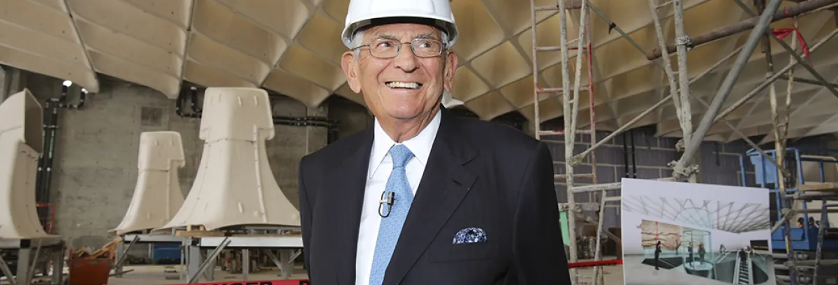 Eli Broad wearing a white hard hat and a dark suit standing at the construction site for The Broad Museum