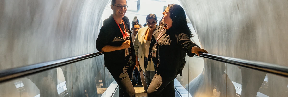 Two tour guides heading up the escalator to the third floor collection galleries with a group behind them