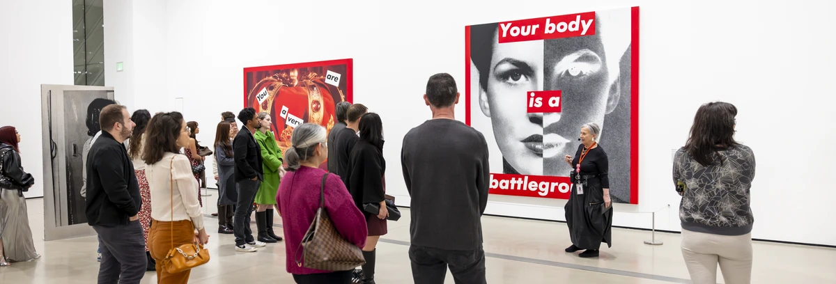 Tour group standing in front of a Barbara Kruger artwork while a tour guide is speaking.