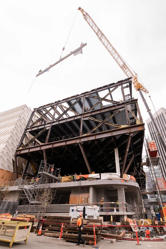 the expansion steel structure, with the final beam above it being lifted by crane into place