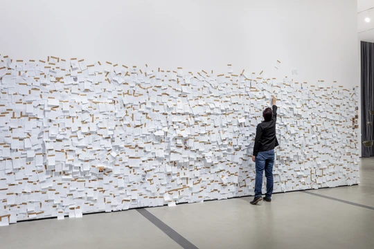 A visitor participating in Yoko Ono's "My Mommy is Beautiful" by writing a note about or to their mother and taping it to the walls.
