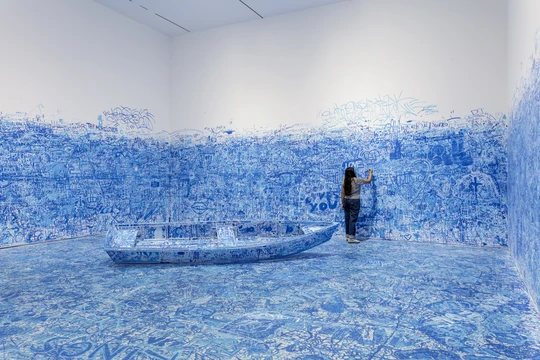 A person inside the room featuring Yoko Ono's Add Colour (Refugee Boat) where visitors are able to draw on the installation and walls with blue and white markers.