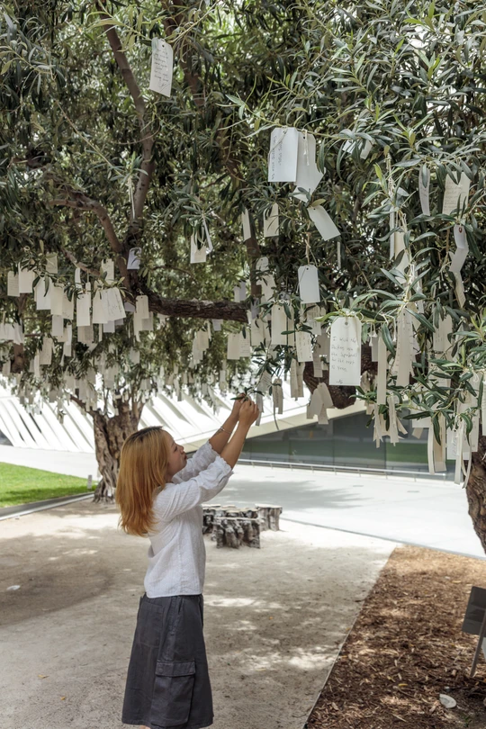 A person tying their wish onto Yoko Ono's Wish Tree for Los Angeles at The Broad