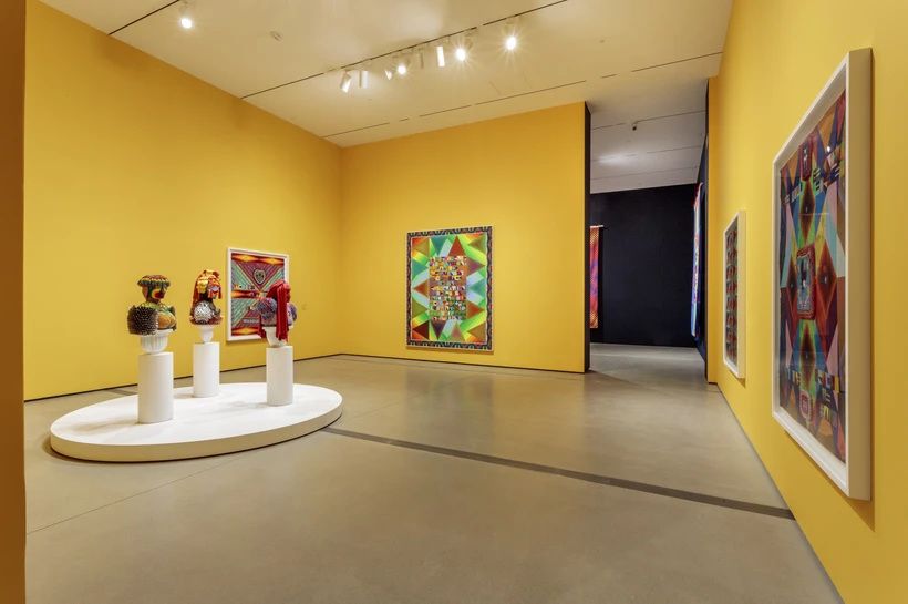 Trio of beaded multi colored busts and three multicolored paintings inside a bright yellow gallery