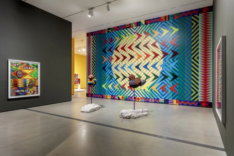 Gallery shot of multicolored beaded bird sculptures against a large multicolored mural