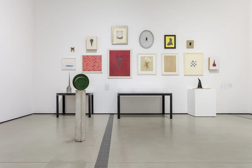 Installation image inside Robert Therrien: This is a Story, featuring multiple paintings and drawings hung on the wall and a few small sculptures