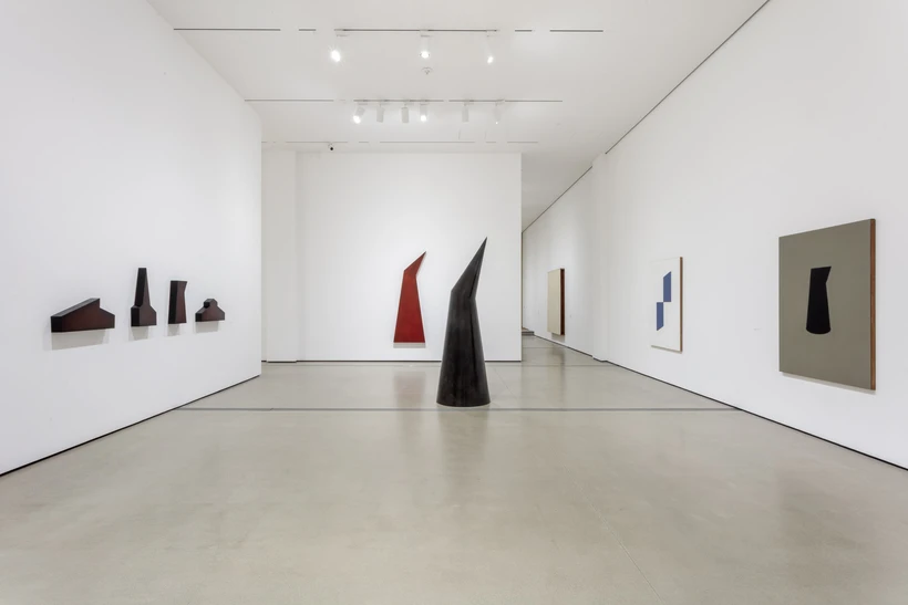 Installation image inside Robert Therrien: This is a Story, featuring one large black sculpture on the floor in the middle of the room and multiple sculptures and paintings on the walls