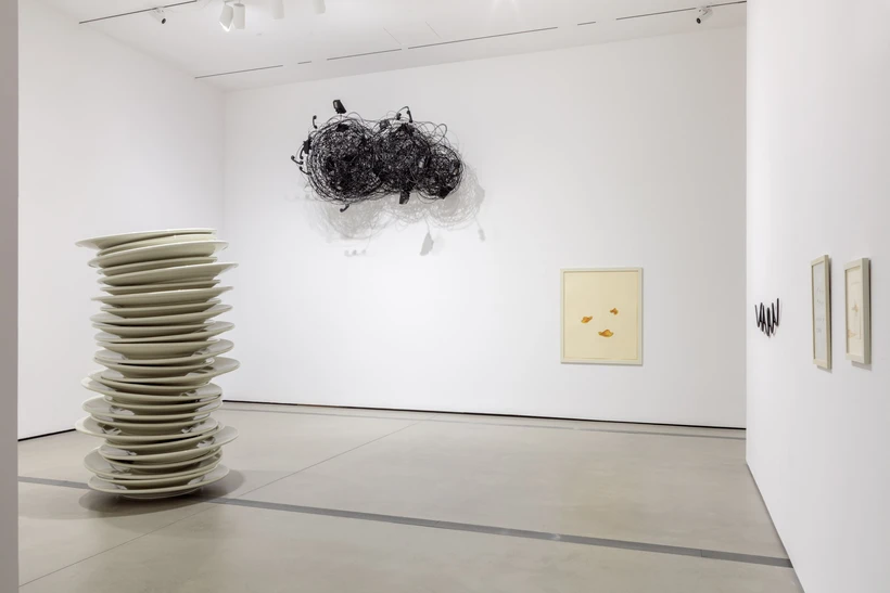 Installation image inside Robert Therrien: This is a Story, featuring a sculpture of a stack of oversized white plates and a cloud made of telephone wires