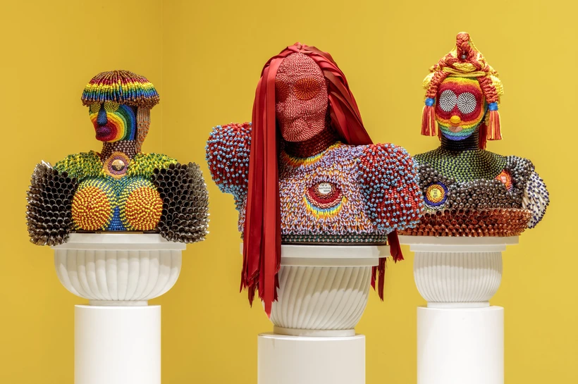 Trio of multi colored beaded busts against a yellow wall