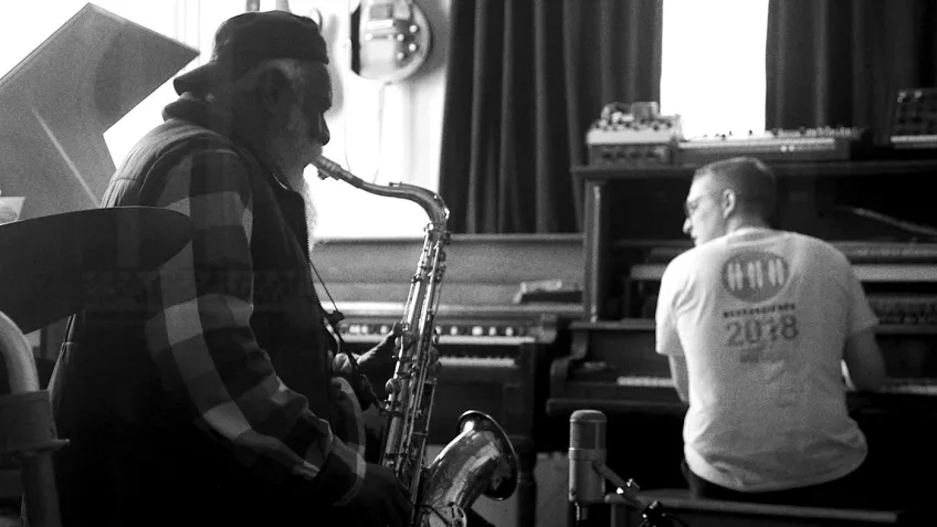Black and white still of a man playing a saxophone and another man on the piano.