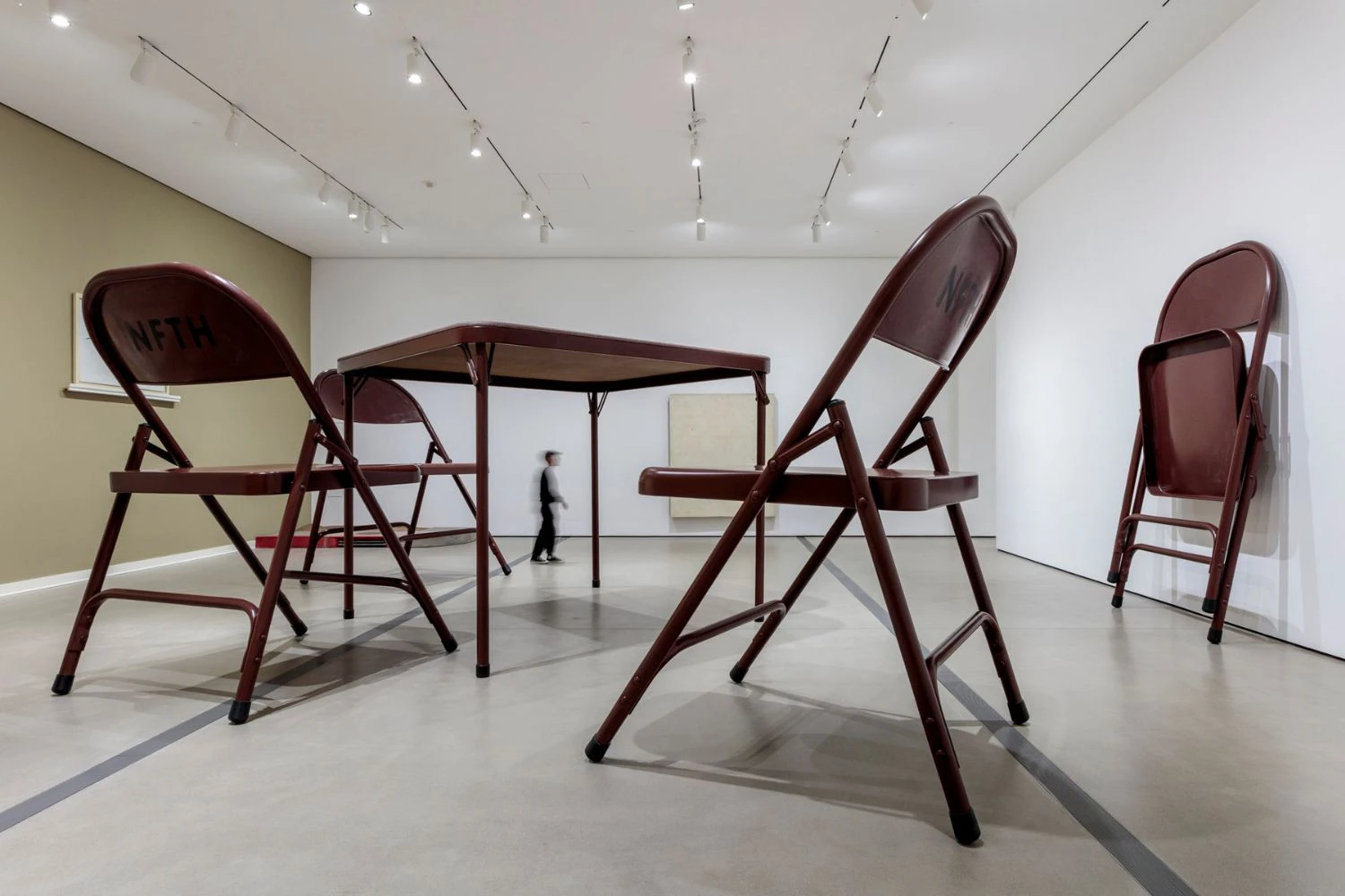 Oversized brown folding table and chairs sculpture by Robert Therrien with a blurry person walking past the artwork to show scale 