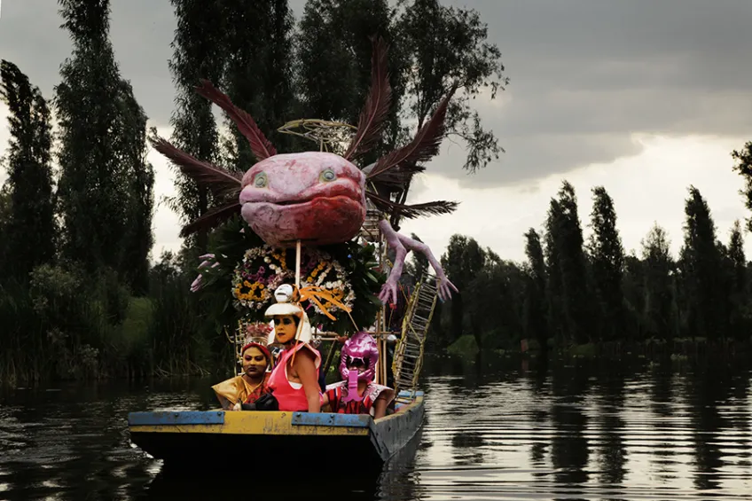 Three women sitting in an axolotl-shaped boat on a pond