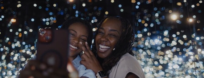 A mom and daughter smiling, taking a selfie inside Yayoi Kusama's Infinity Mirrored Room at The Broad