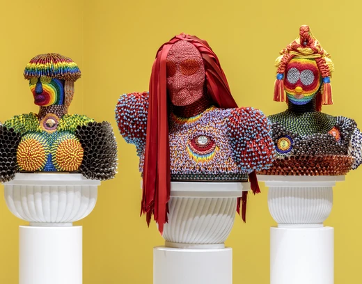 Trio of multicolored trio busts by Jeffrey Gibson against a yellow wall