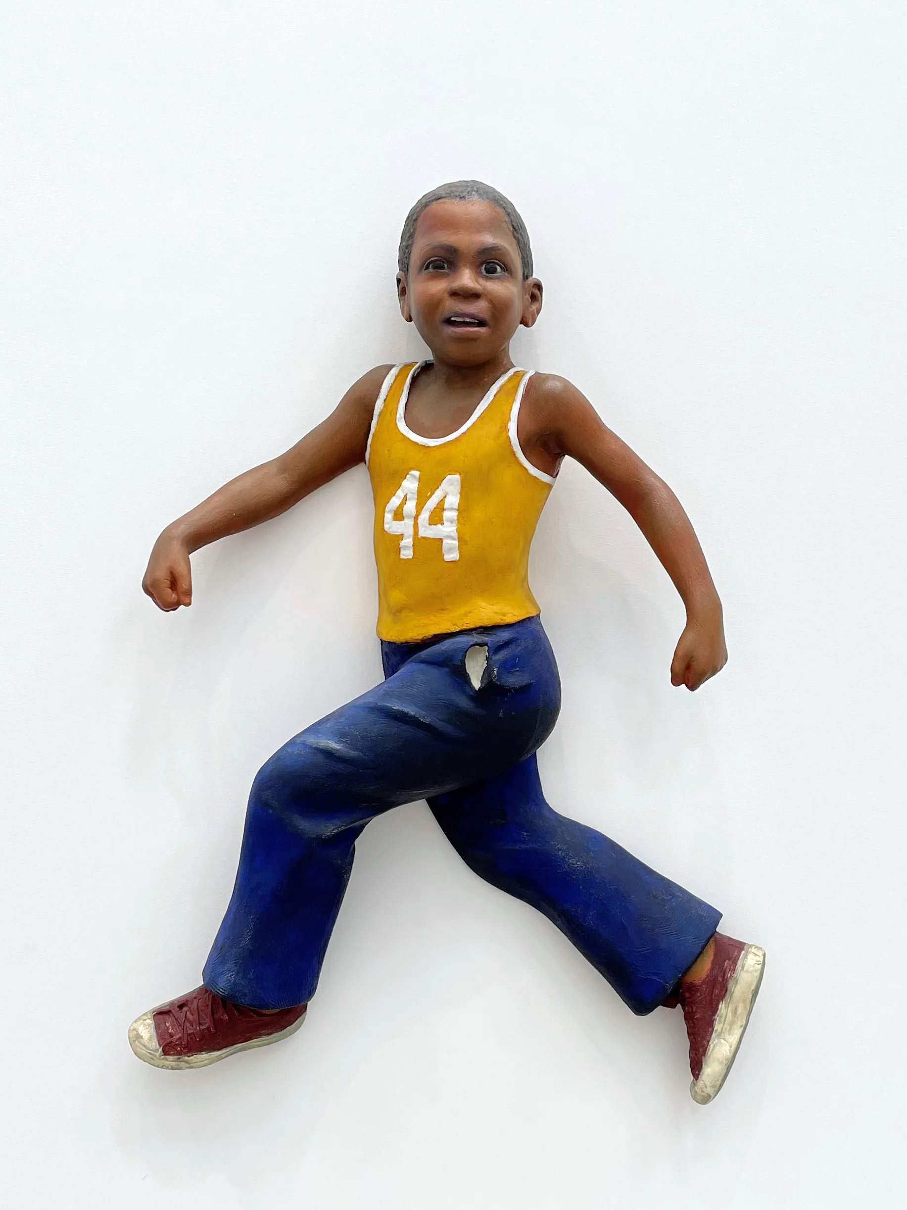 wall sculpture of a boy with a dark skin tone wearing a yellow jersey and blue jeans